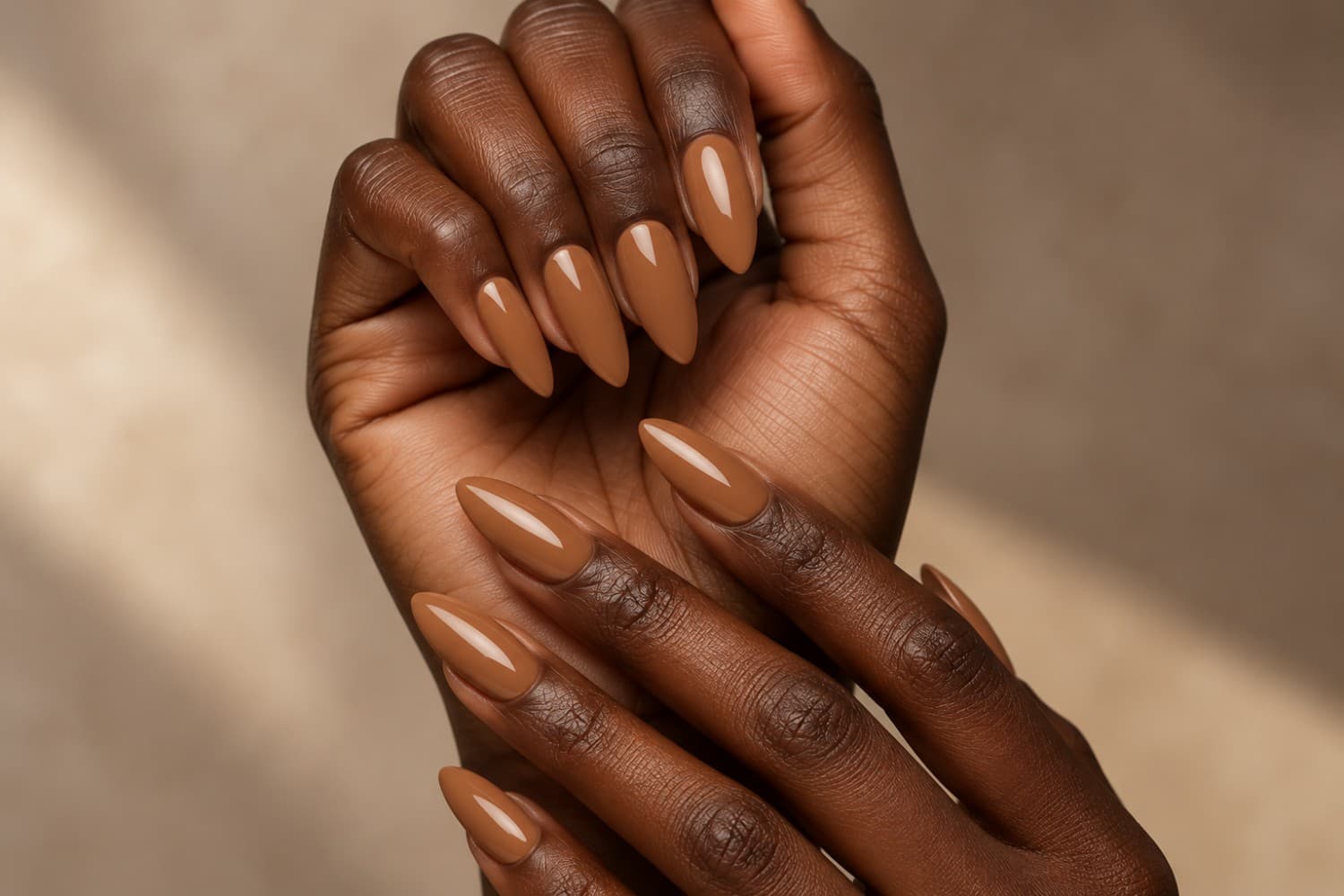 Natural human hands with a soft nude manicure resting on a warm stone table